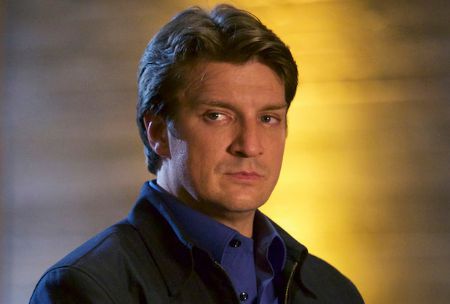Nathan Fillion in a black coat poses for a picture.